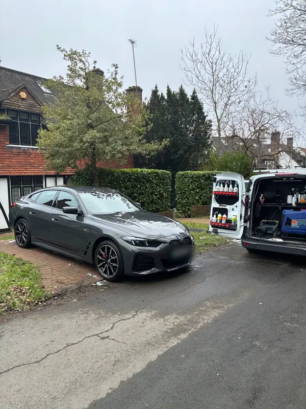 Finished grey BMW i4 on a driveway with the OMVA van open behind it, showing the product racks and generator