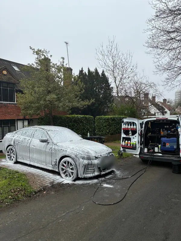 BMW i4 covered in snow foam on a driveway, with the OMVA van and pressure washer alongside